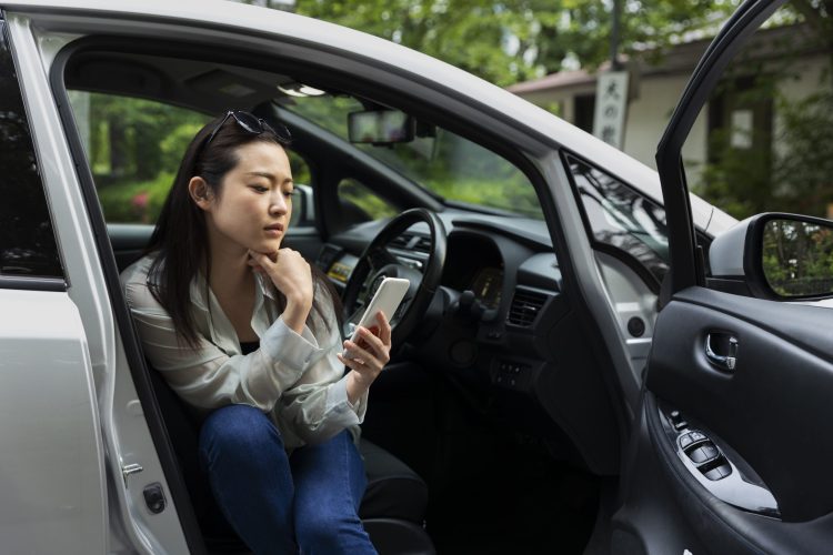 A woman sitting inside an electric car while using her smart phone.