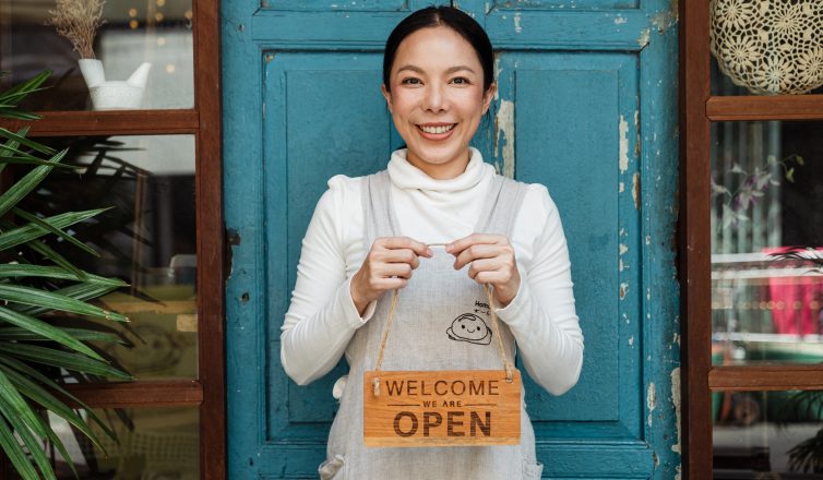 Ethnic female cafe owner showing WELCOME WE ARE OPEN inscription