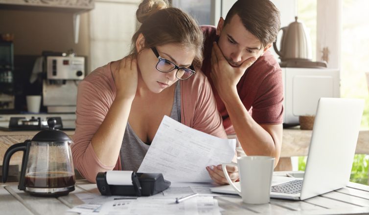 young caucasian family having debt problems, not able to pay out their loan. female in glasses and brunette man studying paper form bank while managing domestic budget together in kitchen interior