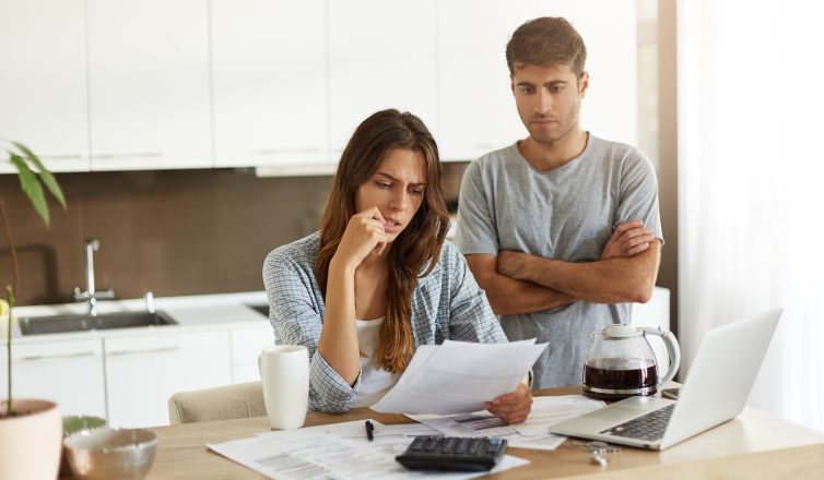 Young man and woman dressed casually looking stressed out while looking at paperwork in the kitchen together