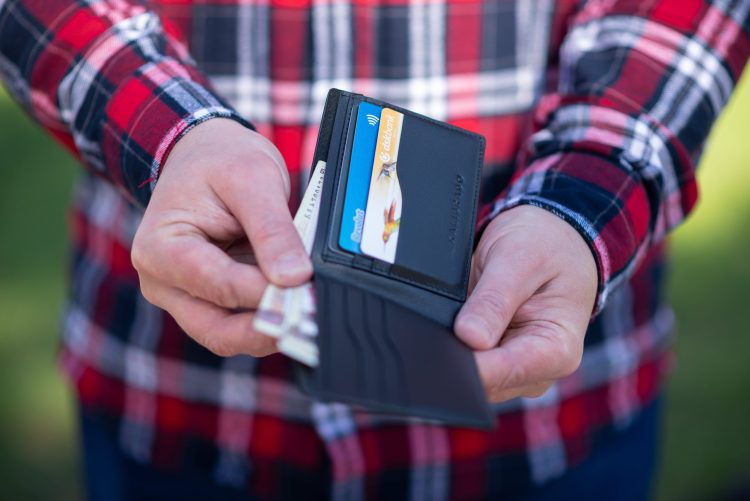 A person taking out a couple of dollar bills from a black bifold wallet